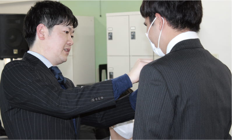 写真:2人の男性が向かい合ってスーツの着こなしを調整している